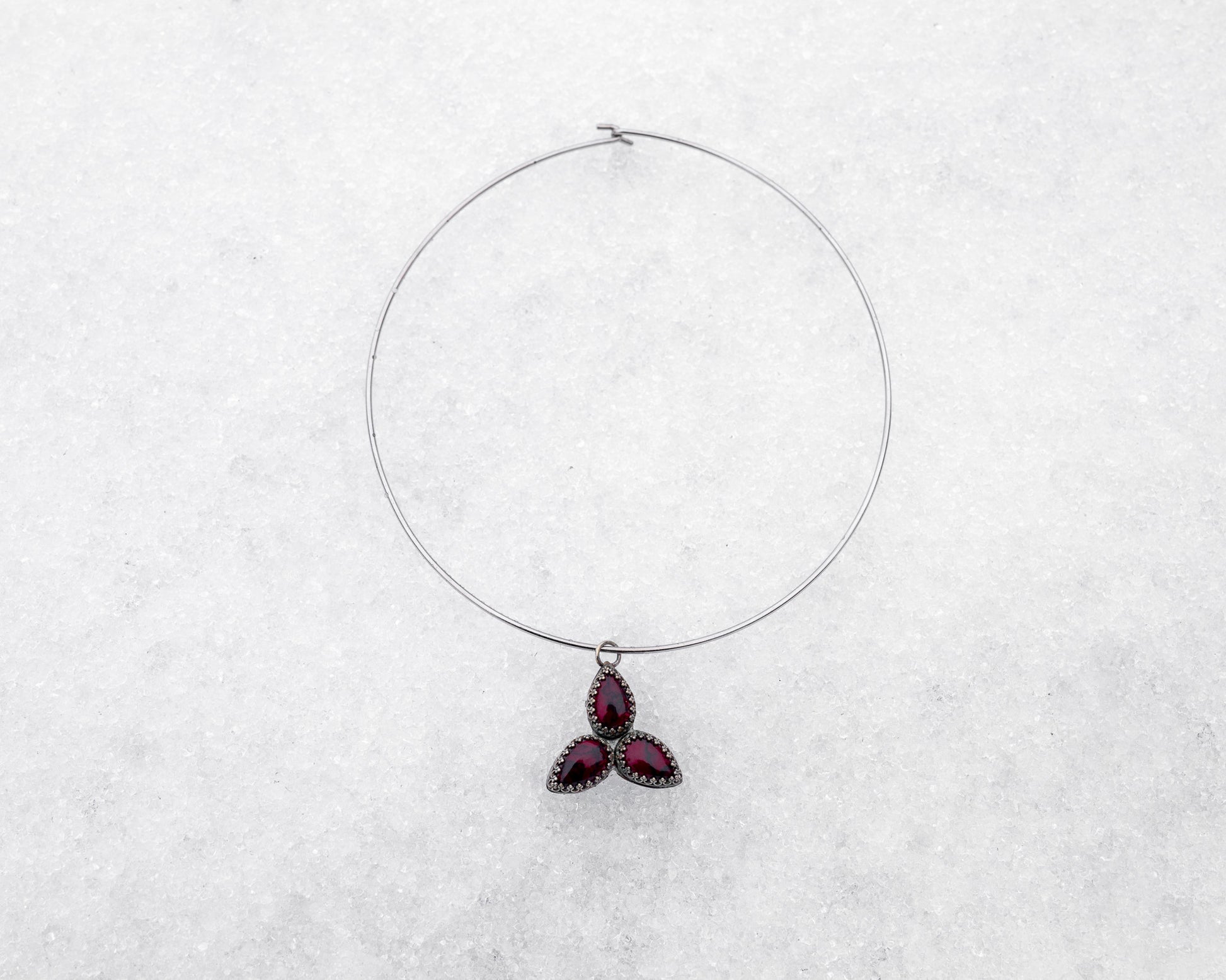 Choker-style wire necklace featuring a trinity formation of three pear-cut bloody bison jasper stones in dark silver bezels. The symmetrical pendant is styled flat on a snowy surface, radiating sacred geometry and ancestral energy.
