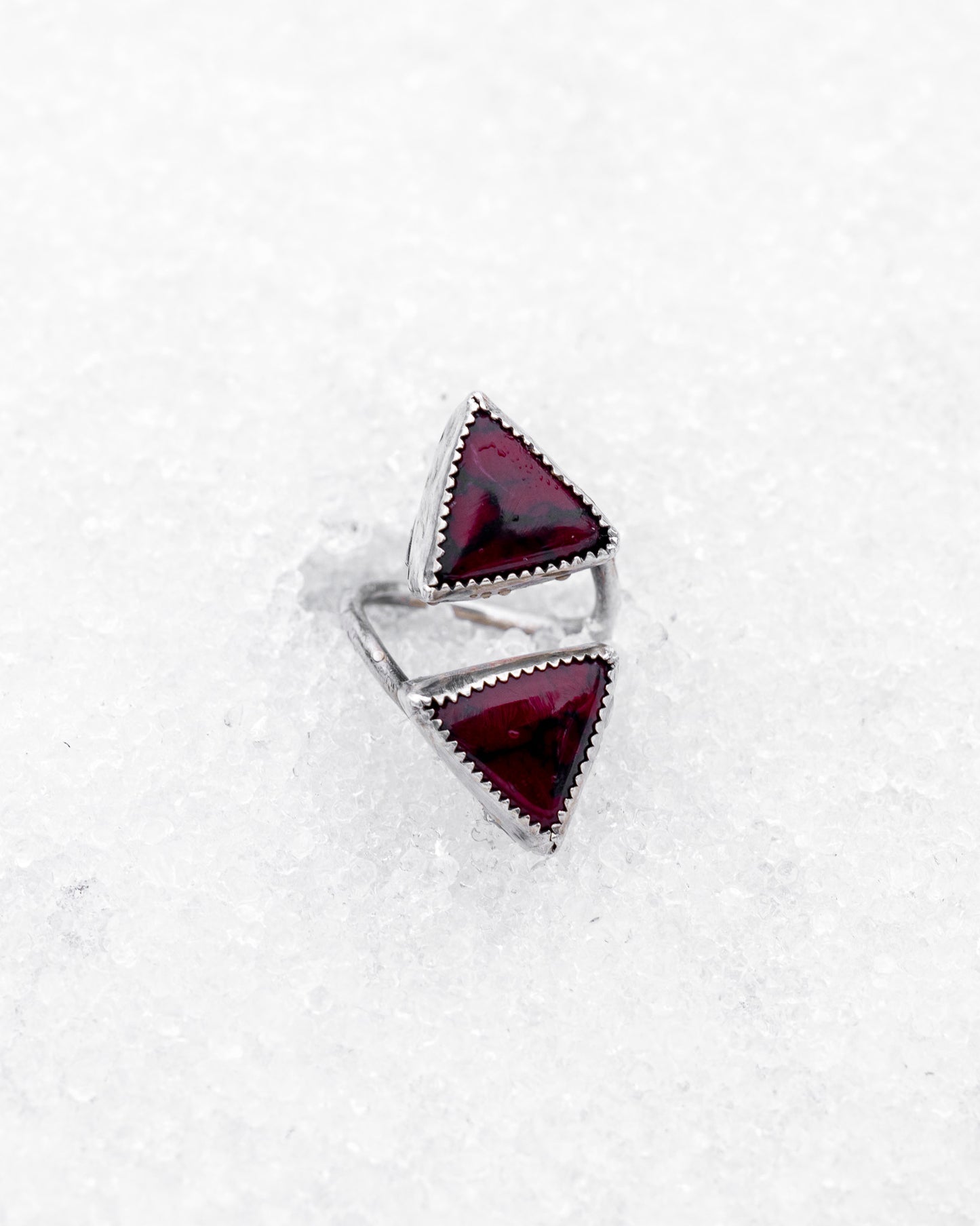 Sterling silver open ring featuring two triangular bloody bison jasper stones pointed inward. The piece rests on icy snow, giving it a mystical, duality-driven appearance with a sharp, ceremonial aesthetic.
