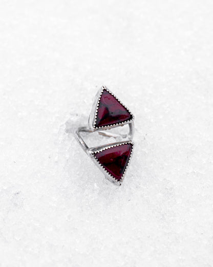 Sterling silver open ring featuring two triangular bloody bison jasper stones pointed inward. The piece rests on icy snow, giving it a mystical, duality-driven appearance with a sharp, ceremonial aesthetic.
