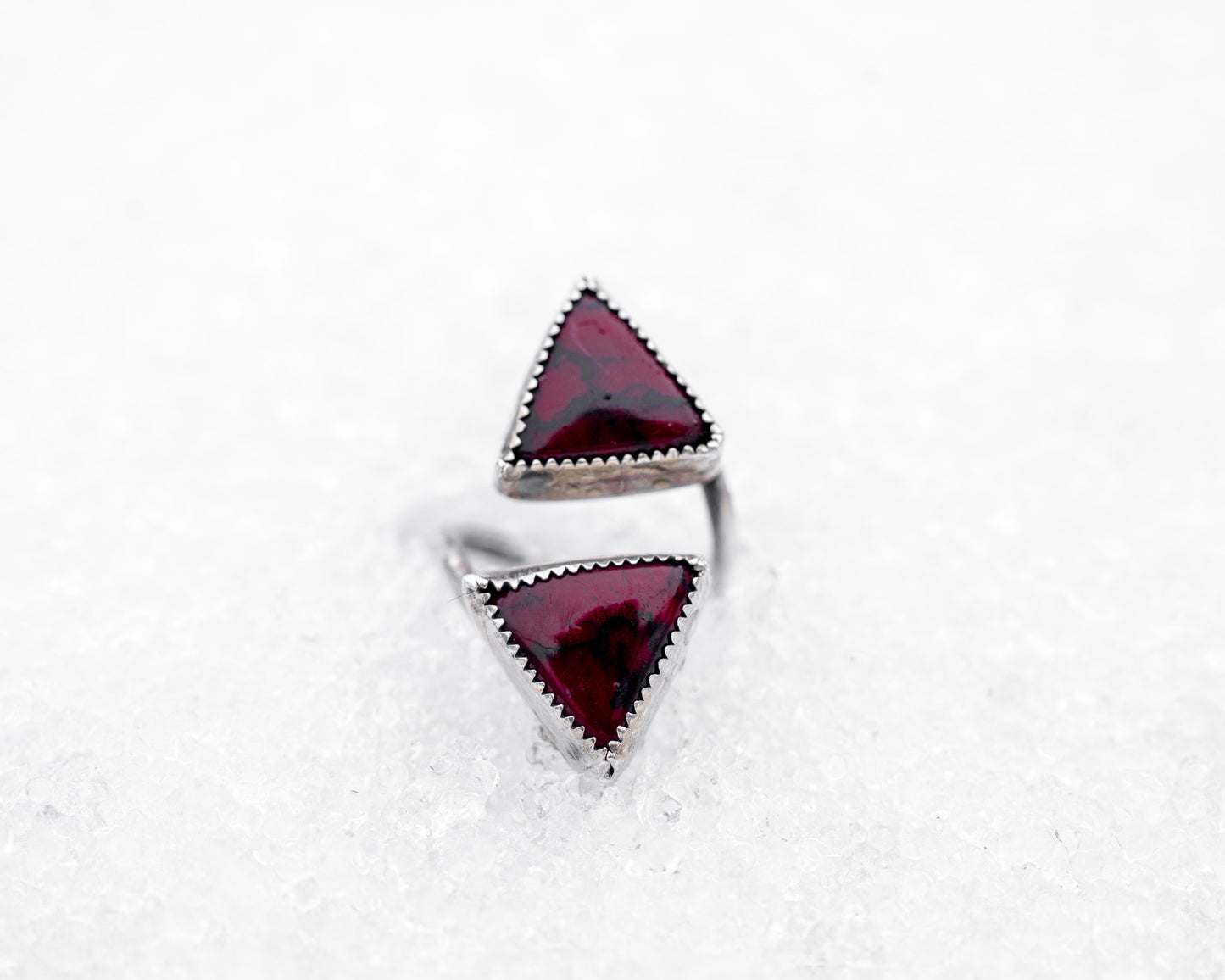 Sterling silver open ring featuring two triangular bloody bison jasper stones pointed inward. The piece rests on icy snow, giving it a mystical, duality-driven appearance with a sharp, ceremonial aesthetic.
