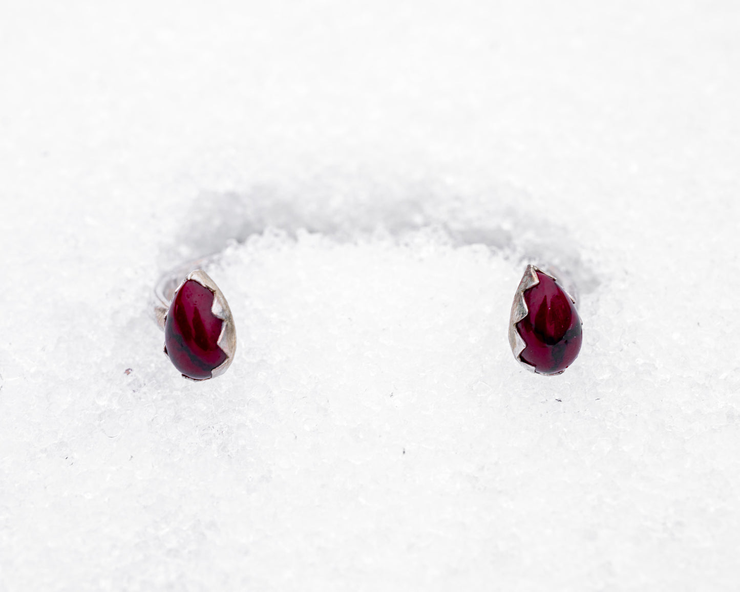 Open sterling silver cuff bracelet with two teardrop-shaped bloody bison jasper stones in jagged fang-like bezels. Photographed resting in white snow, the cuff evokes a fierce, protective energy and vampiric elegance.

